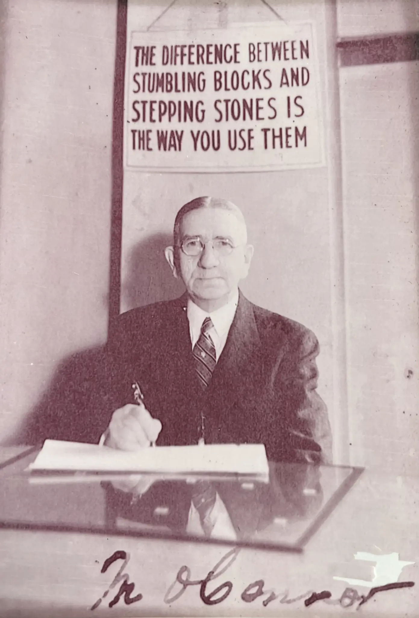 Matthew O'Connor, an executive with Prudential Insurance and the great-grandfather of Brushton Group founder Brendan T. O'Connor, at his desk in Pittsburgh, Pennsylvania, beneath a hand-lettered sign reading The difference between stumbling blocks and stepping stones is the way you use them.
